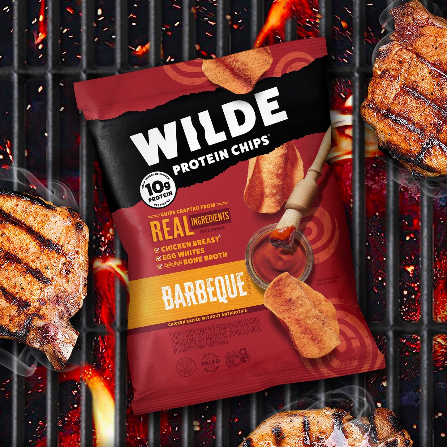 Wilde Protein Chips Barbeque flavor bag on a grill with grilled meat pieces and a brush with barbeque sauce