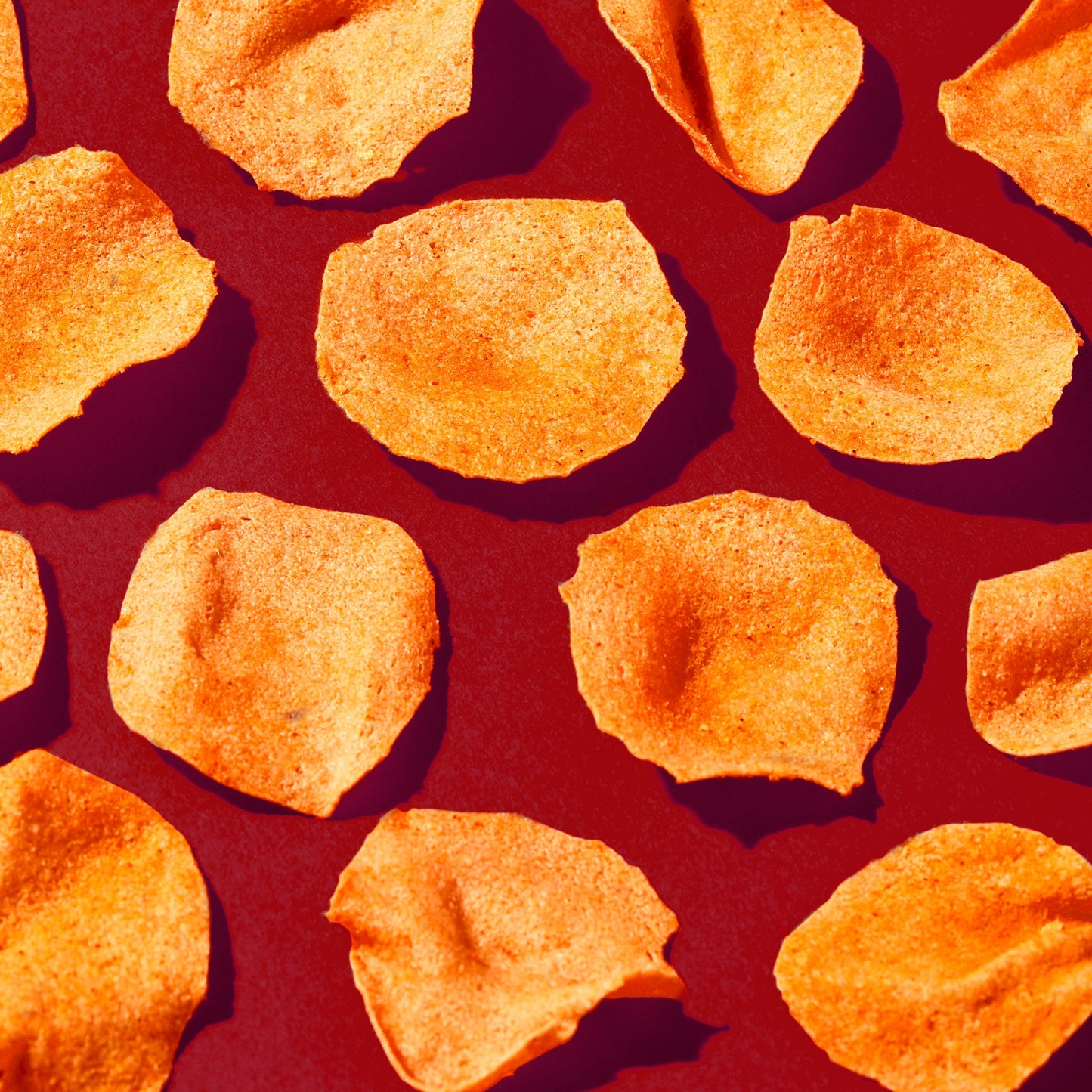 Close-up of barbeque-flavored potato chips scattered on a red surface.