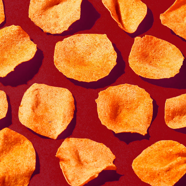 Close-up of barbeque-flavored potato chips scattered on a red surface.